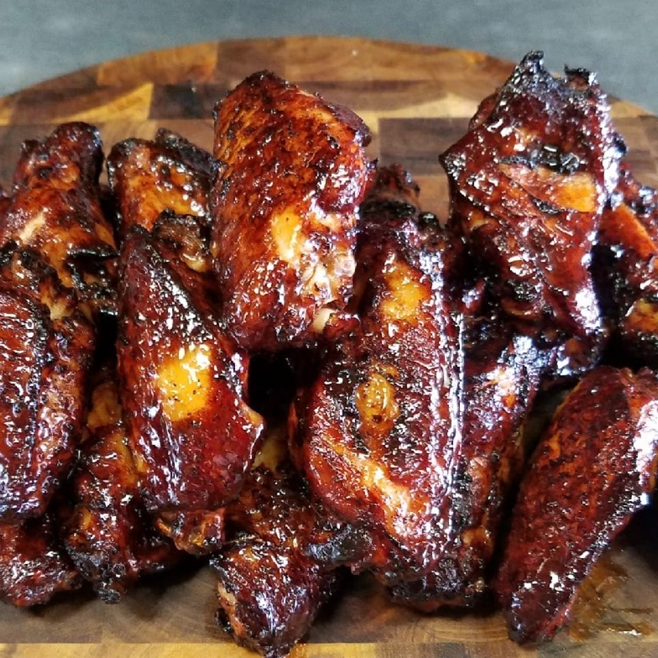 Glazed, charred chicken wings piled on a round wooden serving board.