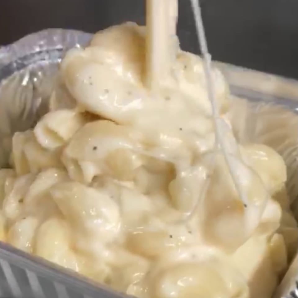 Creamy macaroni and cheese topped with melted cheese in a foil serving tray.