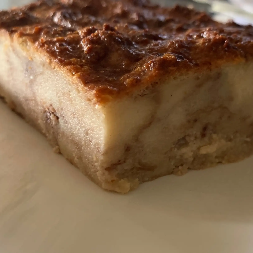 Close-up of a thick rectangular slice of baked custard dessert with a caramelized brown top on a plate.